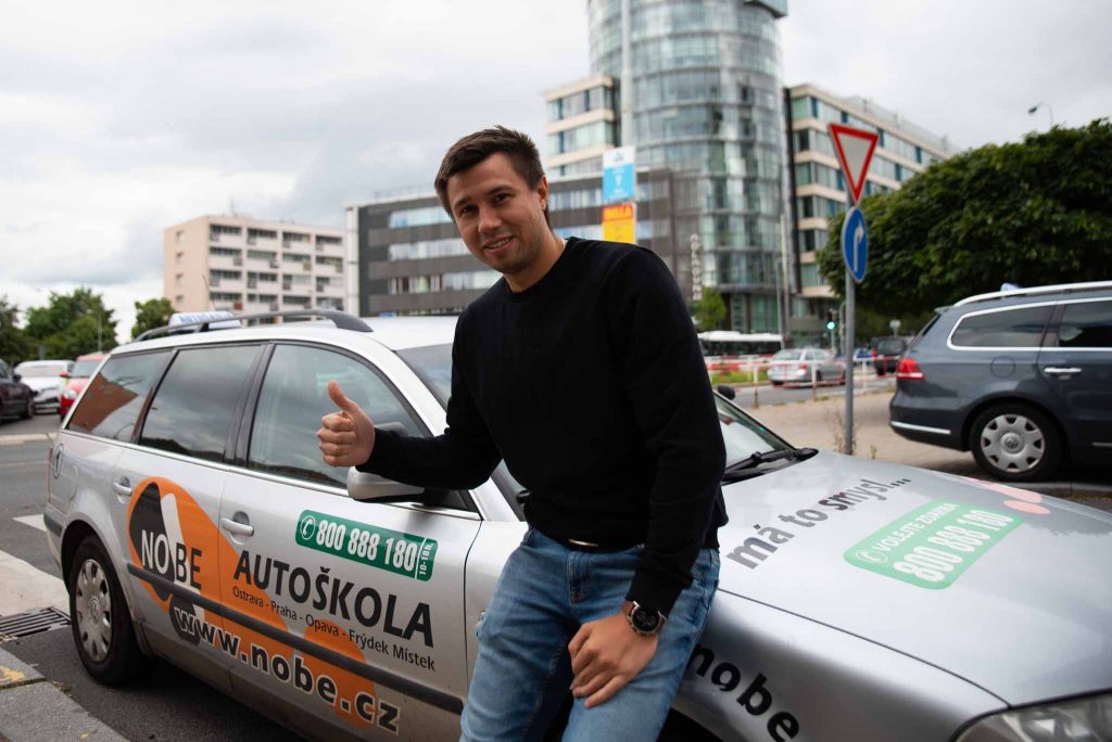 Lektor stojící u výcvikového vozu autoškoly.